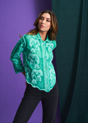 Woman wearing a green embroidered blouse against a purple and green curtain background