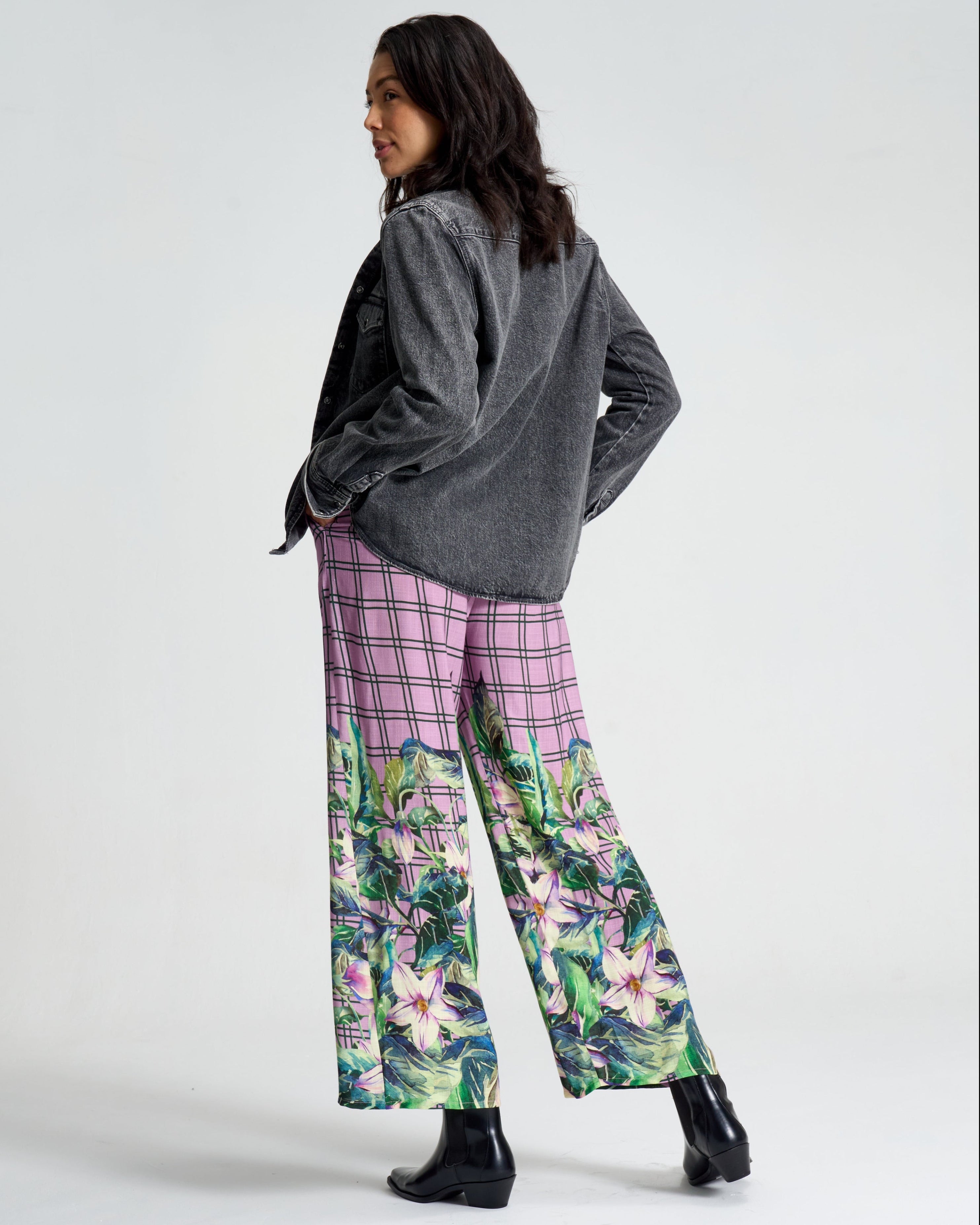 Person wearing a gray sweater and pink floral pants on a white background