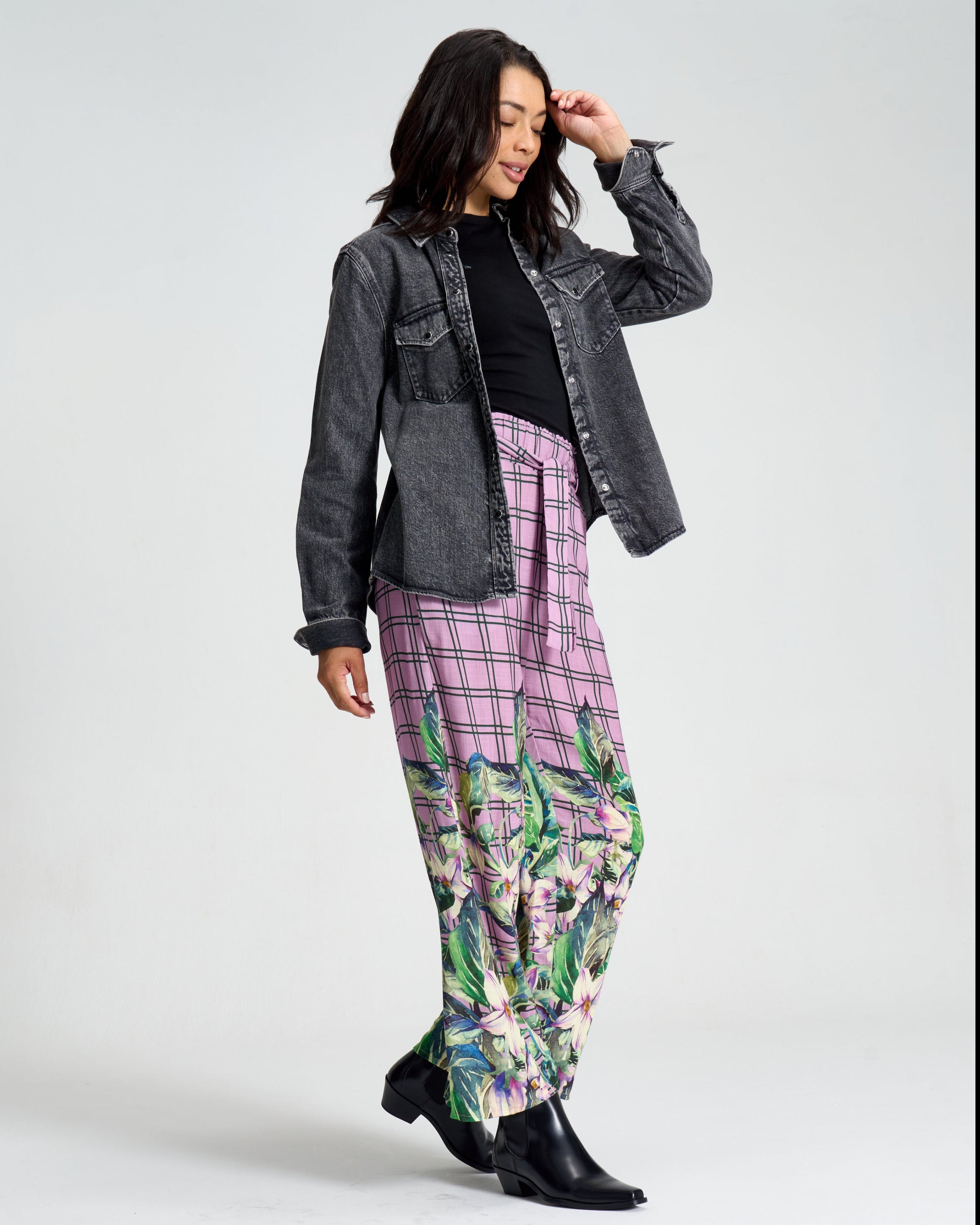 Woman wearing a gray jacket, black top, plaid pants, and floral pants with black shoes on a white background