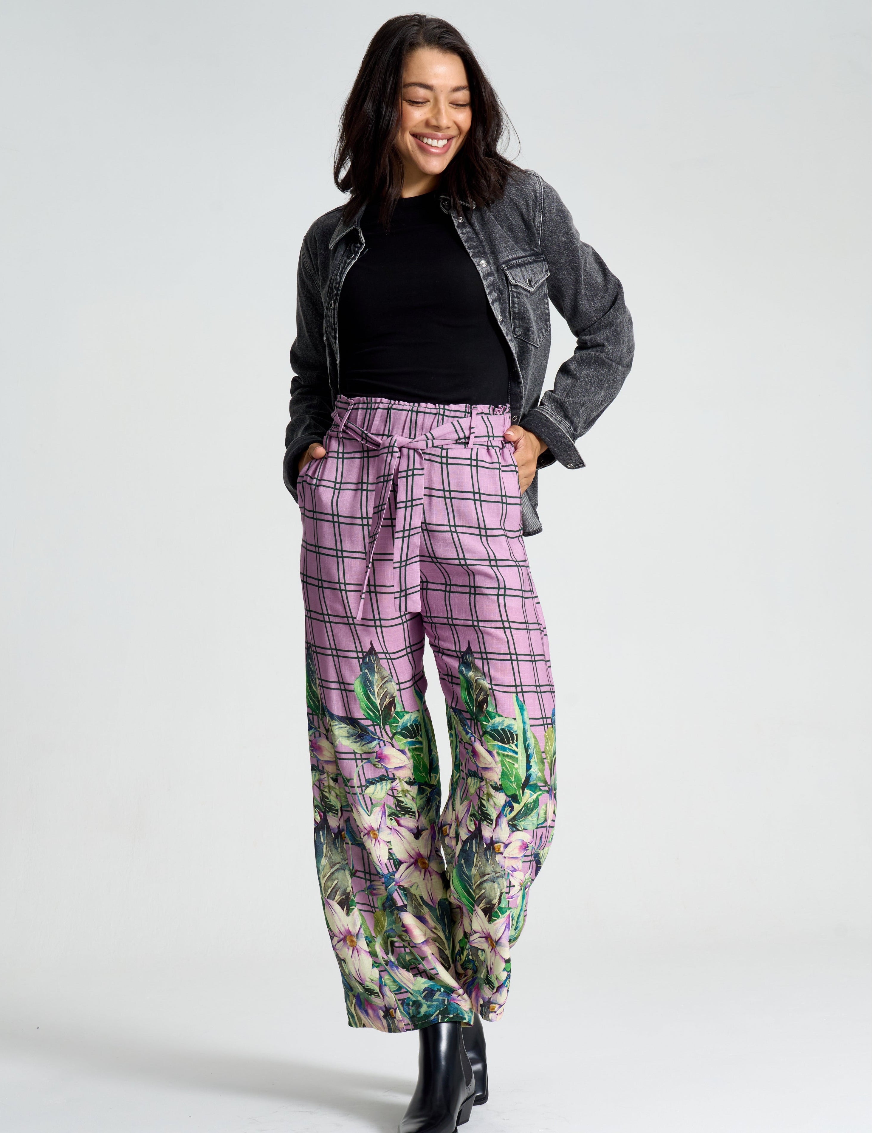Woman wearing a gray jacket, black top, and floral pants on a white background