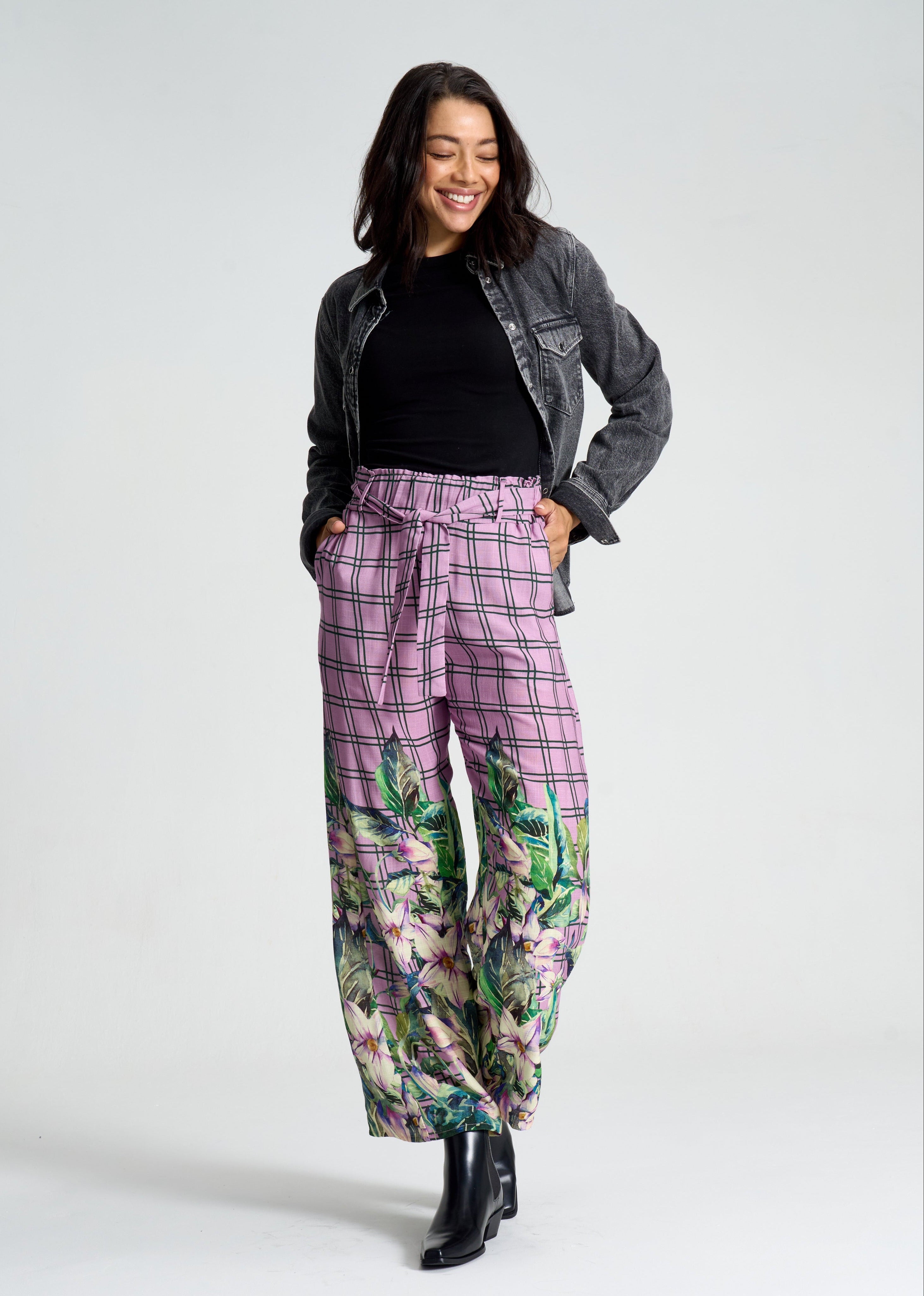 Woman wearing a gray jacket, black top, and floral pants on a white background