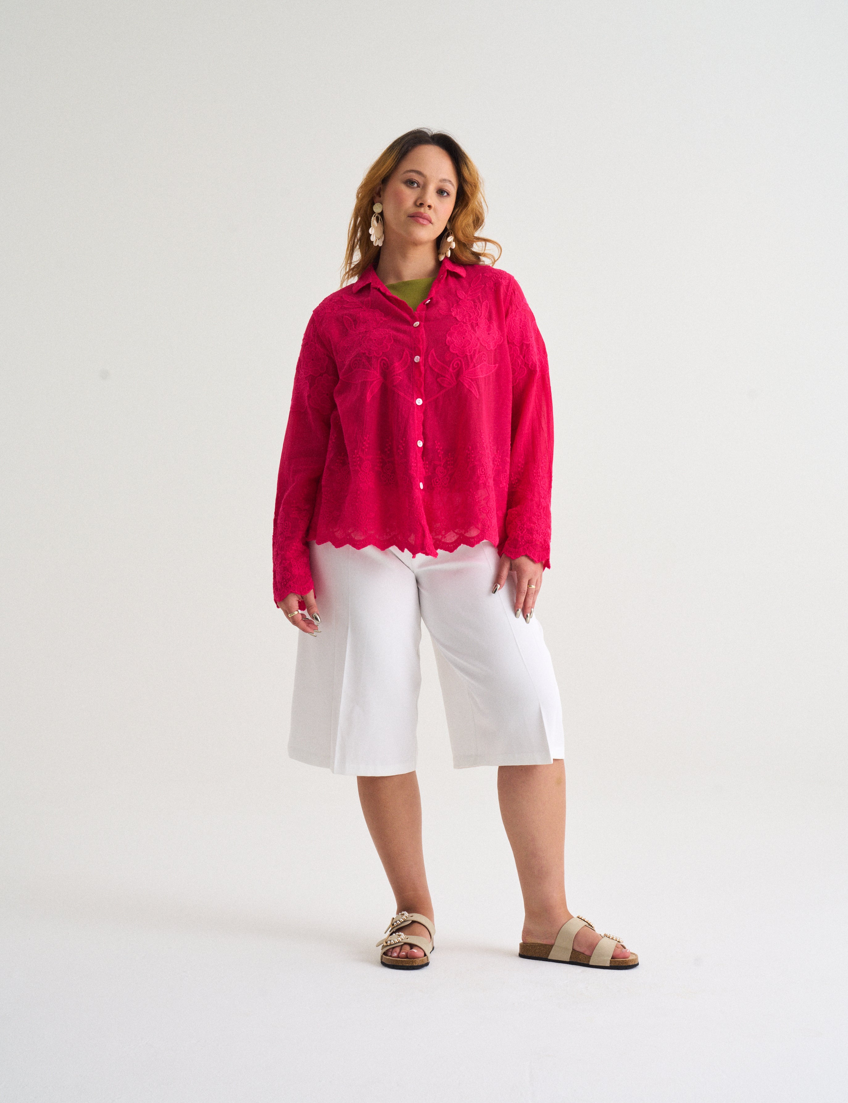 Woman wearing a bright pink shirt and white pants on a white background