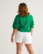 Person wearing a green blouse and white shorts on a plain background