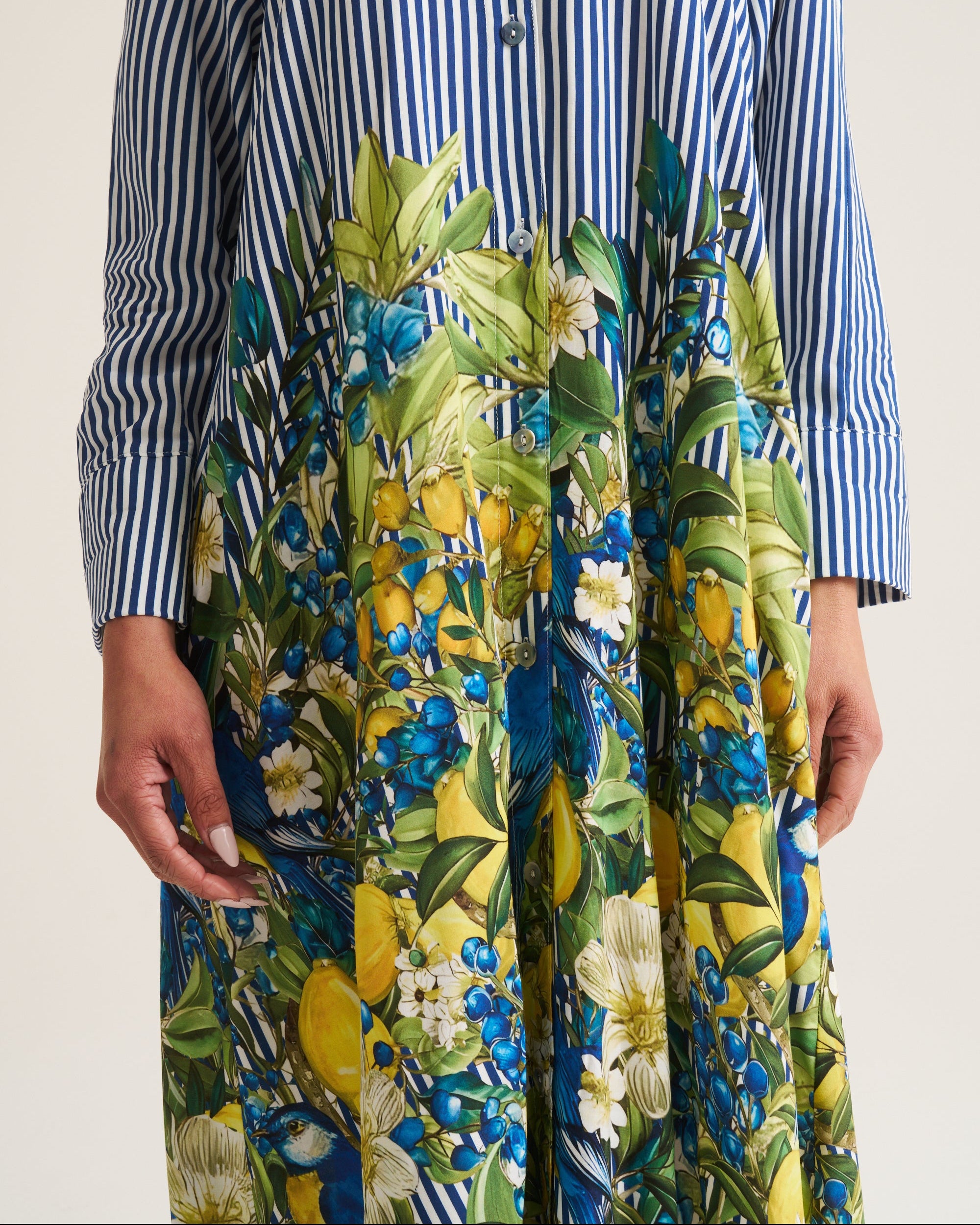 A long-sleeve button-front dress with a blue and white striped upper bodice and a vibrant floral skirt featuring blue, yellow, green, and white botanical patterns.