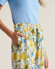 A close-up of a model wearing high-waisted, wide-leg trousers with a yellow lemon and blue floral print on a white background, paired with a light blue top.